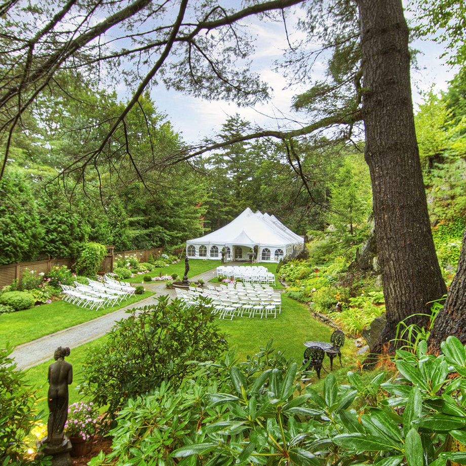 A lush garden surrounding a white tent, rows of chairs, and a fountain