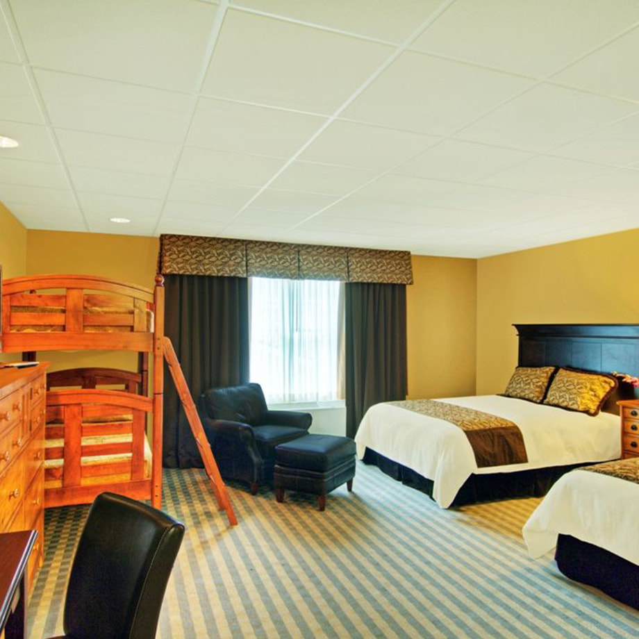 A huge room featuring two queen beds, a leather lounge chair and ottoman, and a wooden bunk bed.
